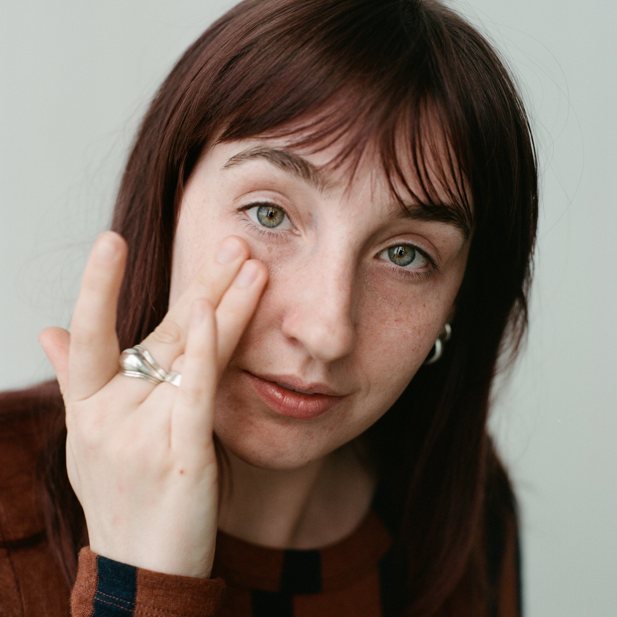 Model pressing two fingers against face on plain background