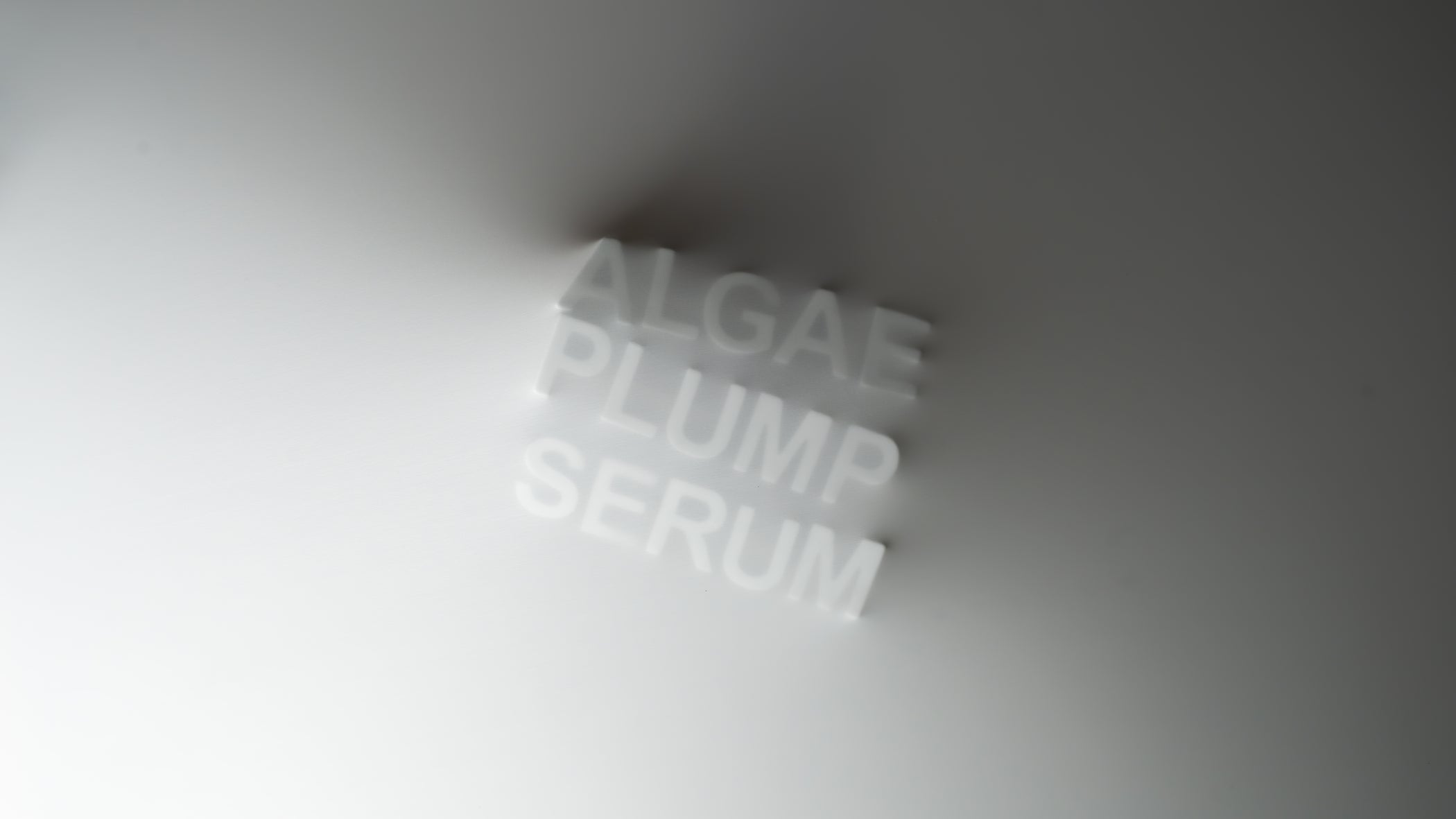 Text 'ALGAE PLUMP SERUM' pushing through a gradient fabric foreground