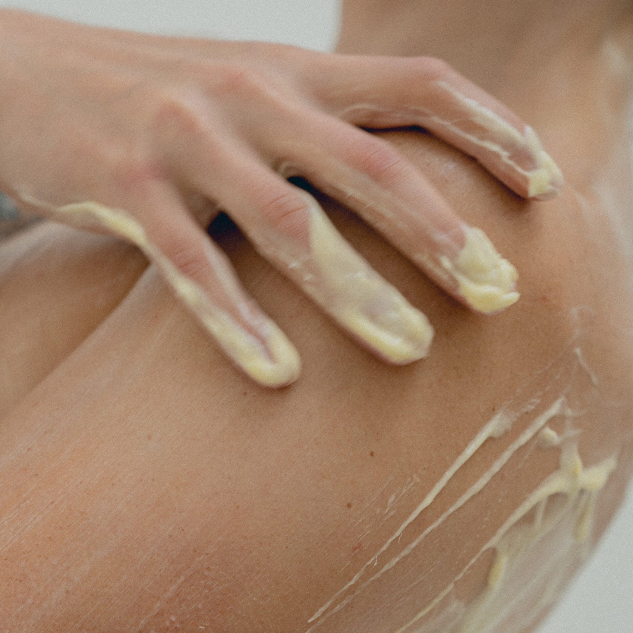 Close-up of model applying yellow lotion to body with hand on shoulder against white background