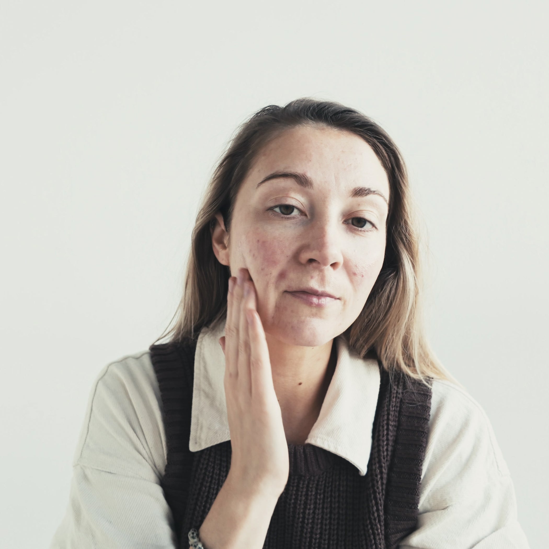 Model pressing fingers against face on plain background